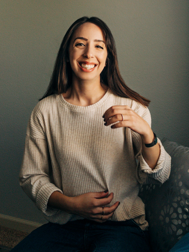 Photo portrait of Belqise, looking at the reader, gesturing as she laughs.