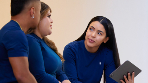 Three Apple Retail team members talking together with one holding an iPad.