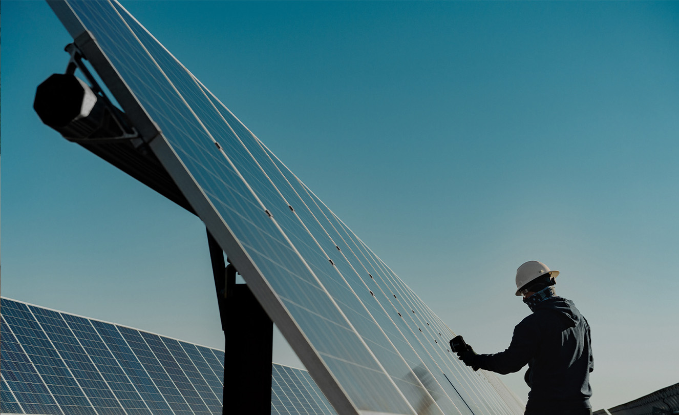 A man in a hardhat working on a large solar panel outside.