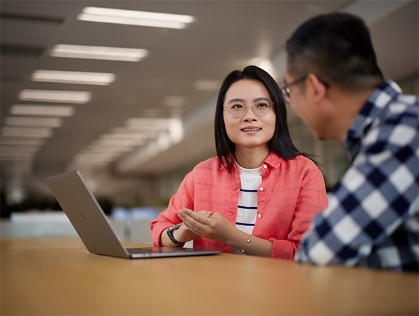 Two seated Apple Software and Services employees discussing work over a MacBook.