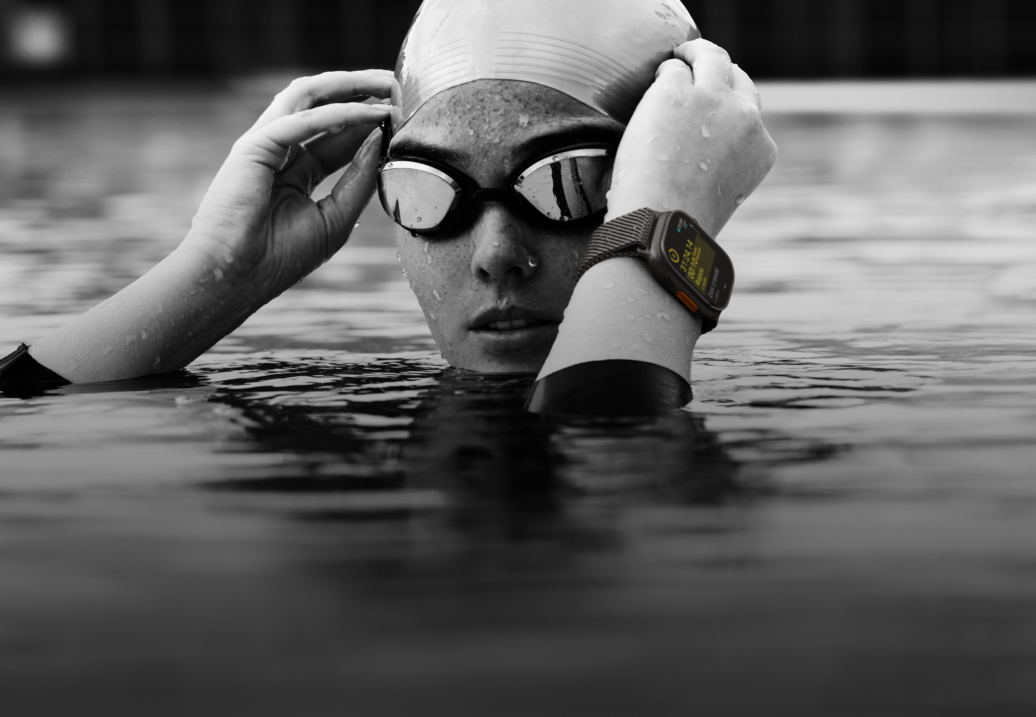 Une personne portant une Apple Watch Ultra 2 dans une piscine a la tête et les mains hors de l’eau pour régler ses lunettes.