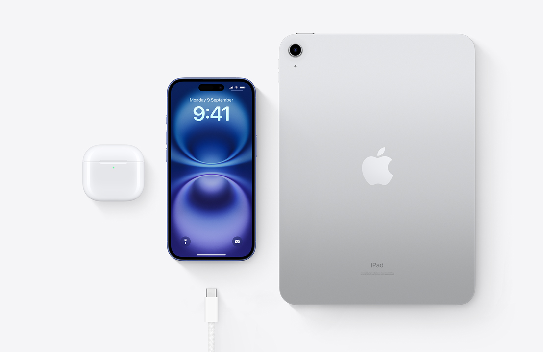 A bird’s-eye view of AirPods Pro, iPhone 16 and an iPad with a USB-C connector to demonstrate how all three devices can be charged using the same USB-C cable.