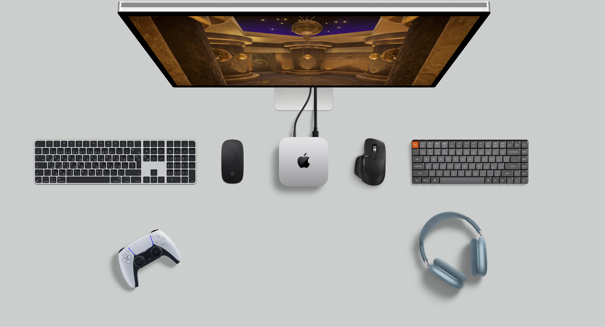 لقطة علوية لجهاز Mac mini فضي اللون ضمن إعداد مكتبي مع شاشة ولوحات مفاتيح لاسلكية وأجهزة ماوس لاسلكية ووحدة تحكم ألعاب وAirPods Max