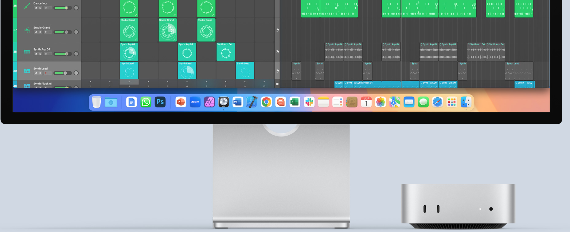 الجهة الأمامية من جهاز Mac mini فضي اللون تعرض المنافذ الأمامية وضوء مؤشر التشغيل، في وضعية مناسبة أسفل شاشة Mac تعرض شاشة مفعمة بالألوان إلى جانب أيقونات التطبيقات في شريط الأيقونات