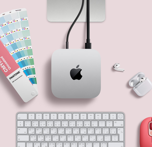 لقطة علوية لجهاز Mac mini فضي اللون ضمن إعداد مكتبي مع سماعات AirPods ولوحة مفاتيح لاسلكية وردية اللون وماوس لاسلكي وردي وعينات ألوان على شكل مروحة