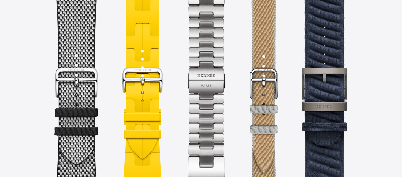 Front view of five Hermès watch bands showing a Noir/Écru (black/white) Toile H Single Tour, a Sun (yellow) Kilim Single Tour, a Satiné Grand H, a Kraft/Bleu Glacier (tan/ice blue) Twill Jump Attelage Single Tour, and a Bleu Nuit (navy blue) En Mer.